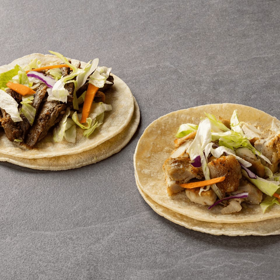 Two B & C Teriyaki tacos, one with beef and one with chicken, on a gray surface.