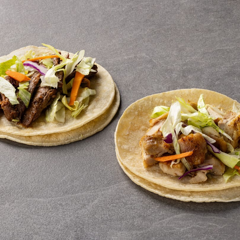 Two B & C Teriyaki tacos, one with beef and one with chicken, on a gray surface.